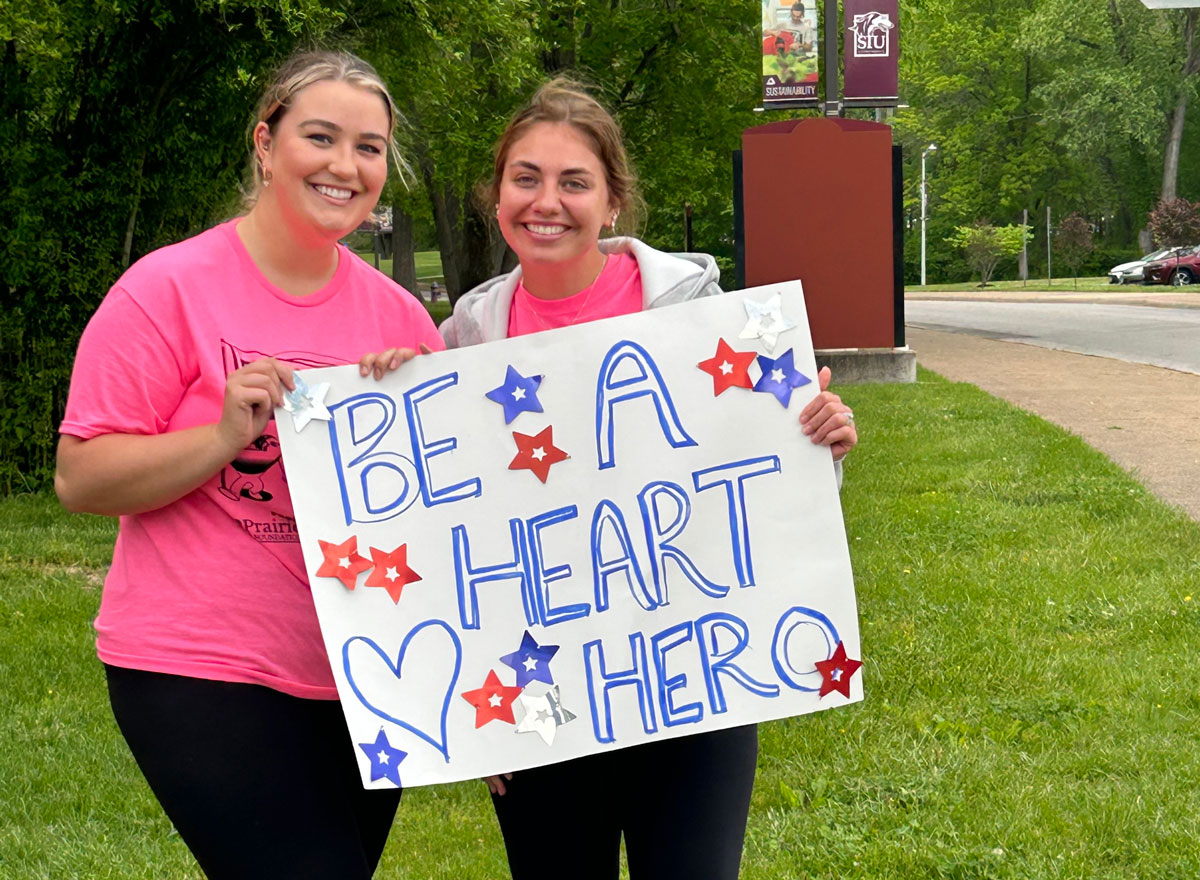 Two young women hold a sign that says Be a Heart Hero