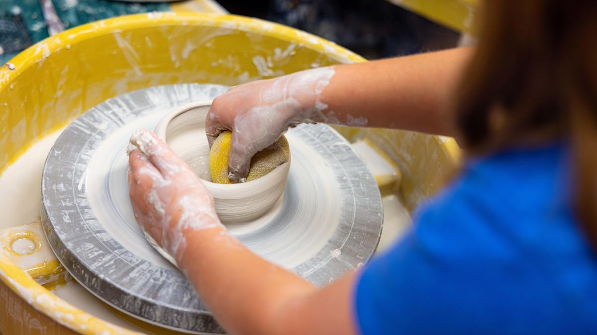 Hands are shaping clay on a pottery wheel.