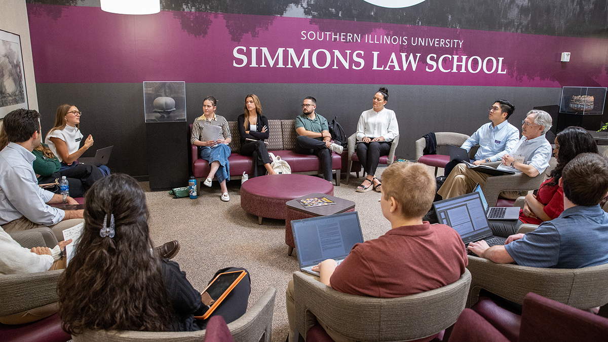 A group of law and medical students are seated in a room, having a discussion. On the wall behind them it reads Southern Illinois University Simmons Law School.
