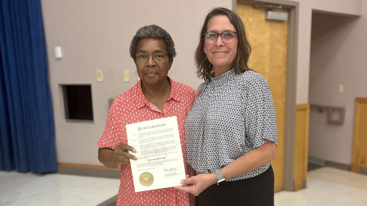 Two women stop for a photo. One is holding a piece of paper.