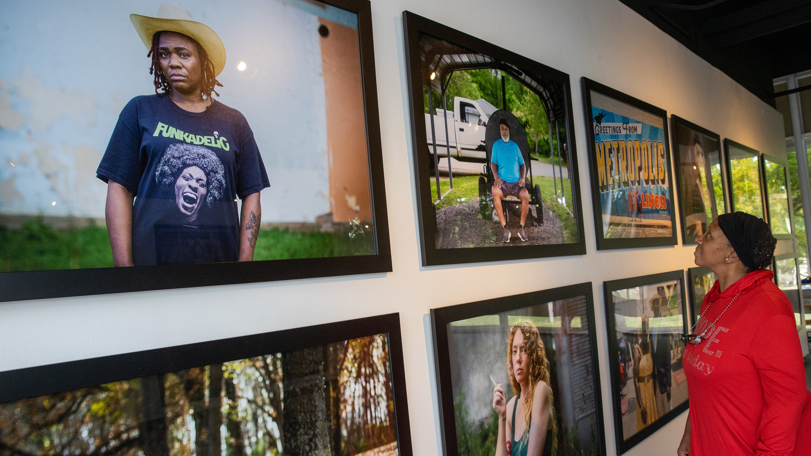 A woman stands in front of a gallery wall admiring the photos hung there.