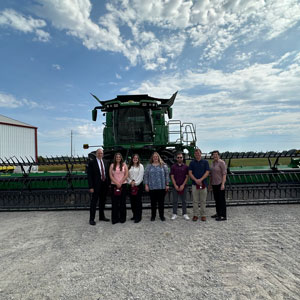 President Mahony and guests at University Farms. They are standing in front of a combine.