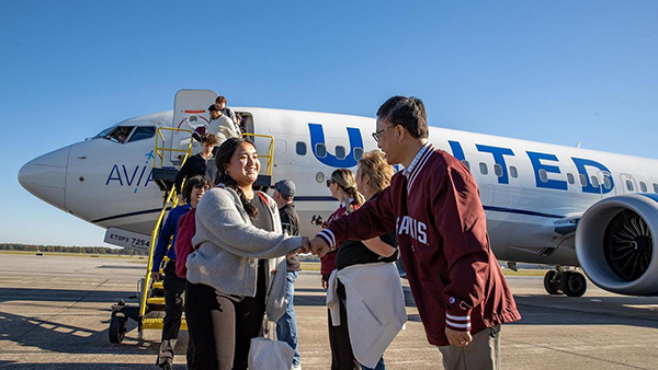 A man is greeting people as they exit an airplane.