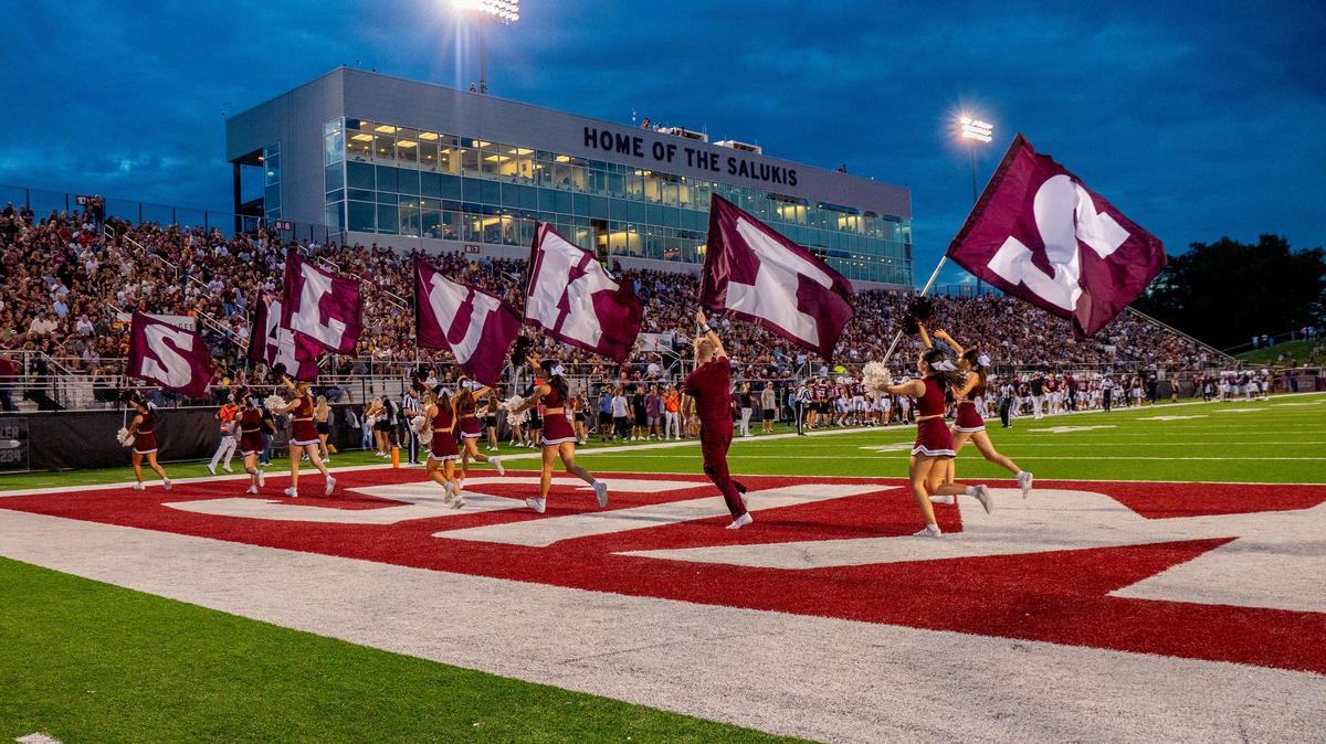 Saluki football game as the cheerleaders run past with flag banners that spell out Salukis.