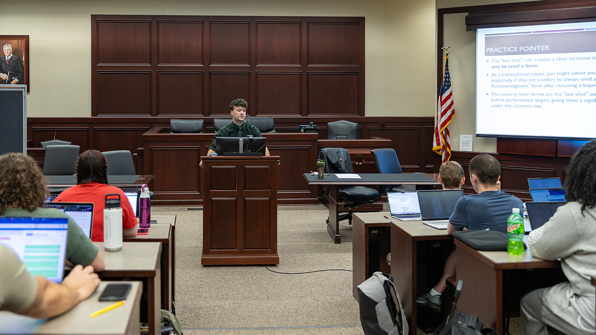 A man is standing at a podium, speaking to a class.