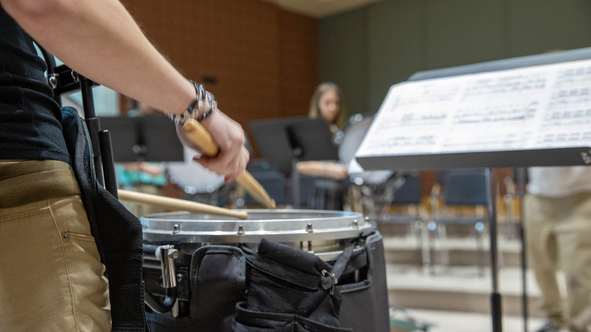 Close up image of a person playing a drum. Sheet music is seen in the background.