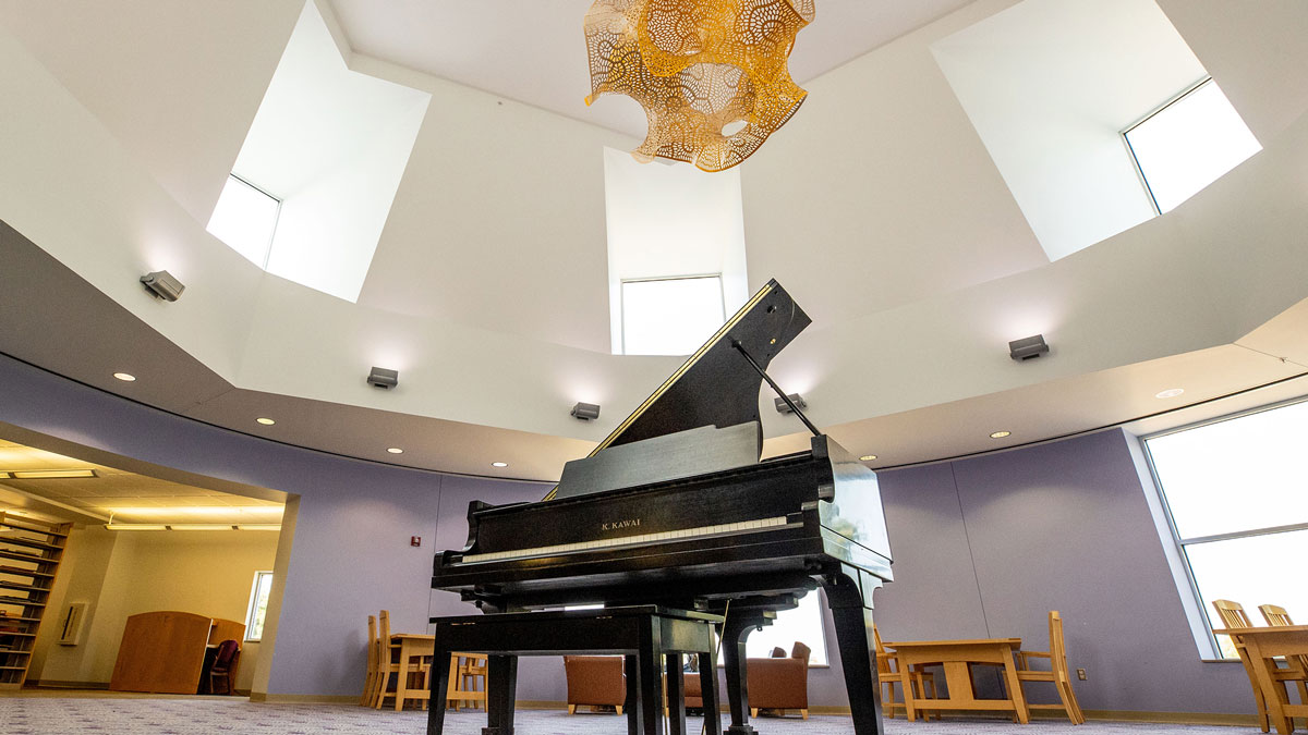 A grand piano in the middle of a large room. Above it hangs a yellow gyroid.