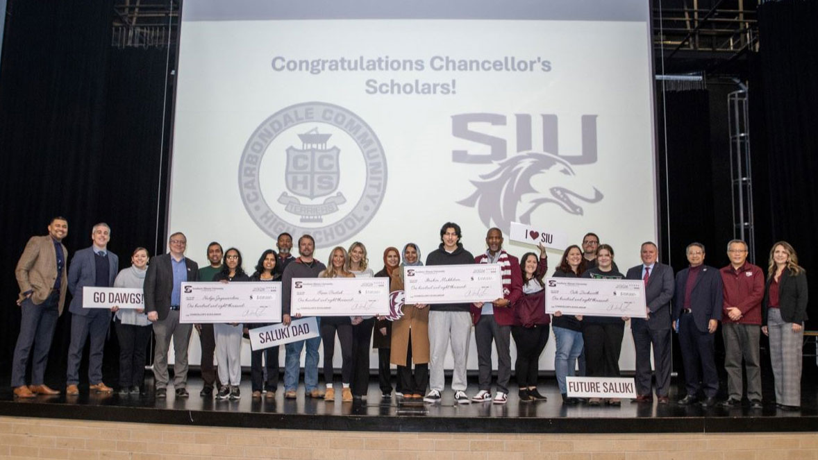 Chancellor Lane celebrates with some recipients of the Chancellor's Scholarships at Carbondale Community High School. The screen behind them says Congratulations Chancellor's Scholars.