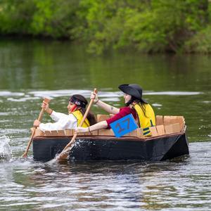 Two young women, dressed as pirates, paddle their cardboard boat.