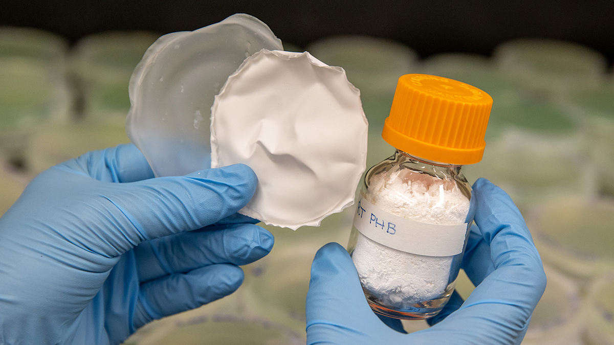 Gloved hands hold plastic pieces and a vial.