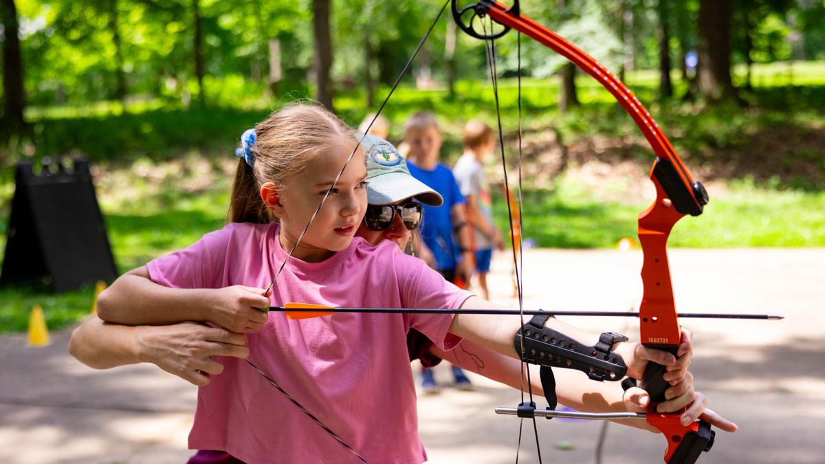 A child is assisted with shooting a bow and arrow.