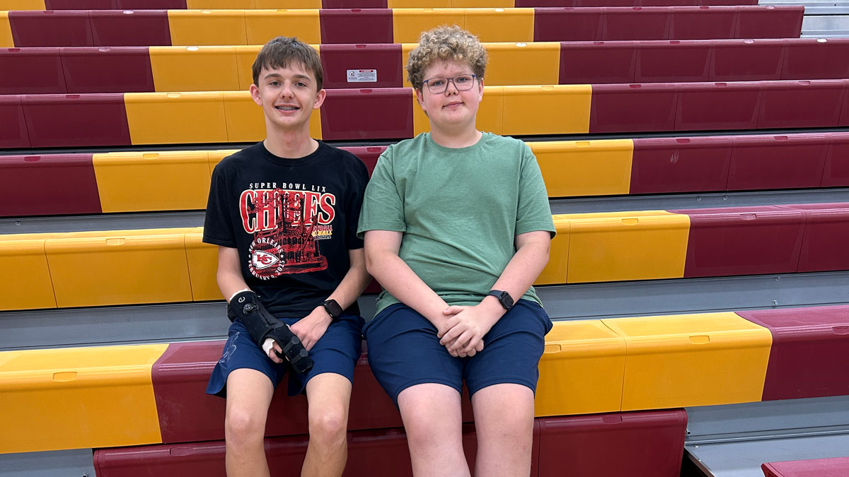 Two boys are seated on bleachers in a gym.