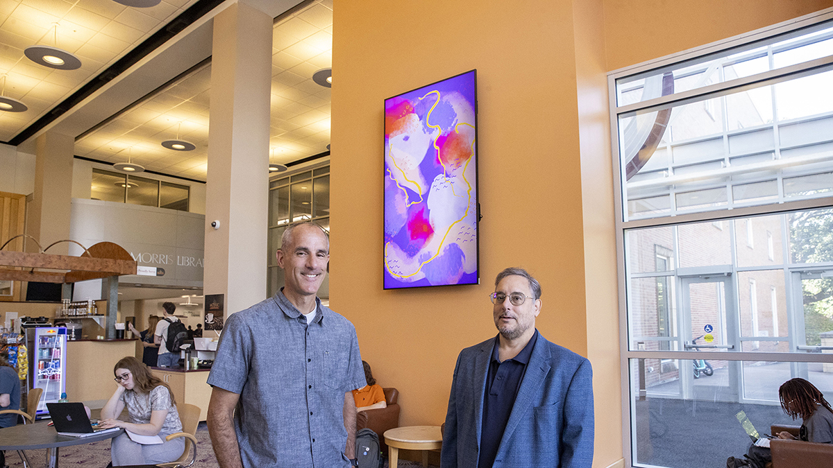 Mark Pease and William Walters stand in front of a 7-foot-high LED display board.